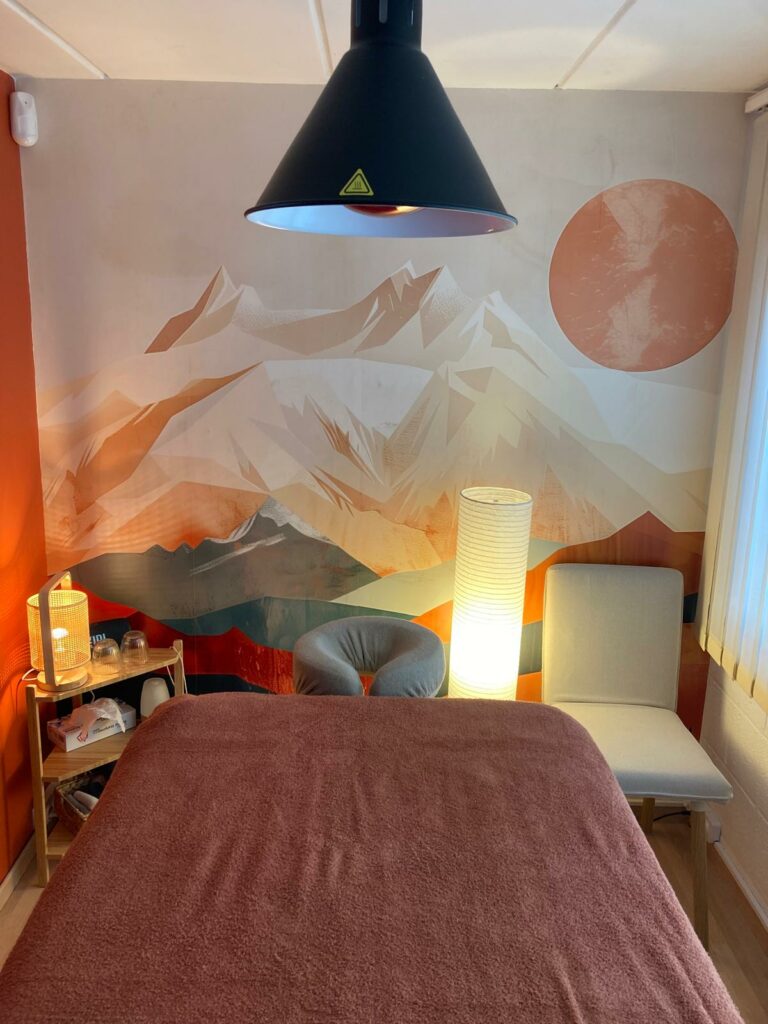 Salle de massage avec table, fresque murale et ambiance tamisée